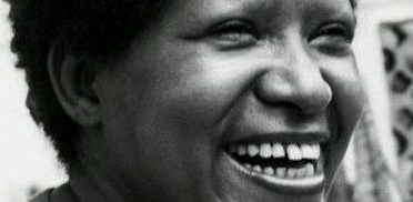 Foto em preto e branco de Lélia Gonzalez, uma mulher negra e de cabelos curtos e crespos. Ela sorri.