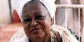 Foto de Mãe Beata, uma mulher negra, que sorri e olha para a foto.